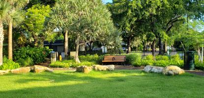 Beautiful sunny morning, blue sky and trees in the background, grassy area with rocks and a bench